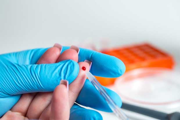 Лаборант в синих медицинских перчатках берет из пальца кровь девушки для анализа