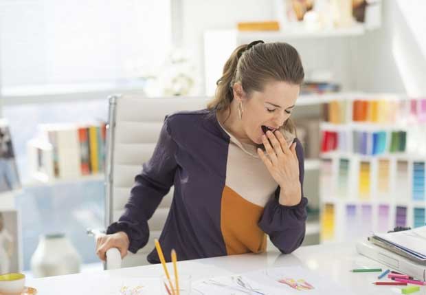 Женщина в возрасте сильно зевает на рабочем месте во время трудового дня
