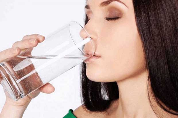 Из-за возникновения сухости во рту девушка пьет много воды из стакана