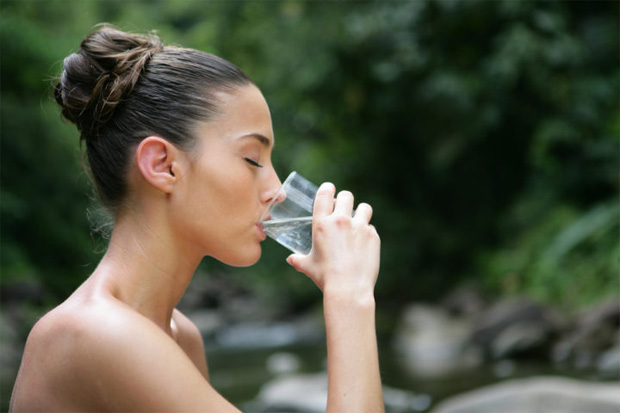 Девушка на природе пьет много воды из прозрачного высокого стакана
