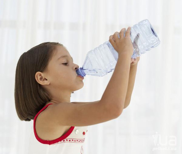 Девочка в комнате пьет много воды из большой пластиковой бутылки