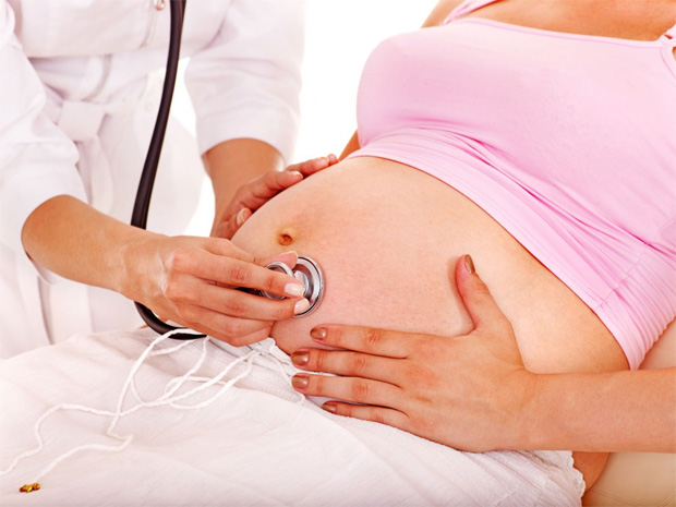 Врач в белом халате слушает стетоскопом сердцебиение ребенка в утробе матери
